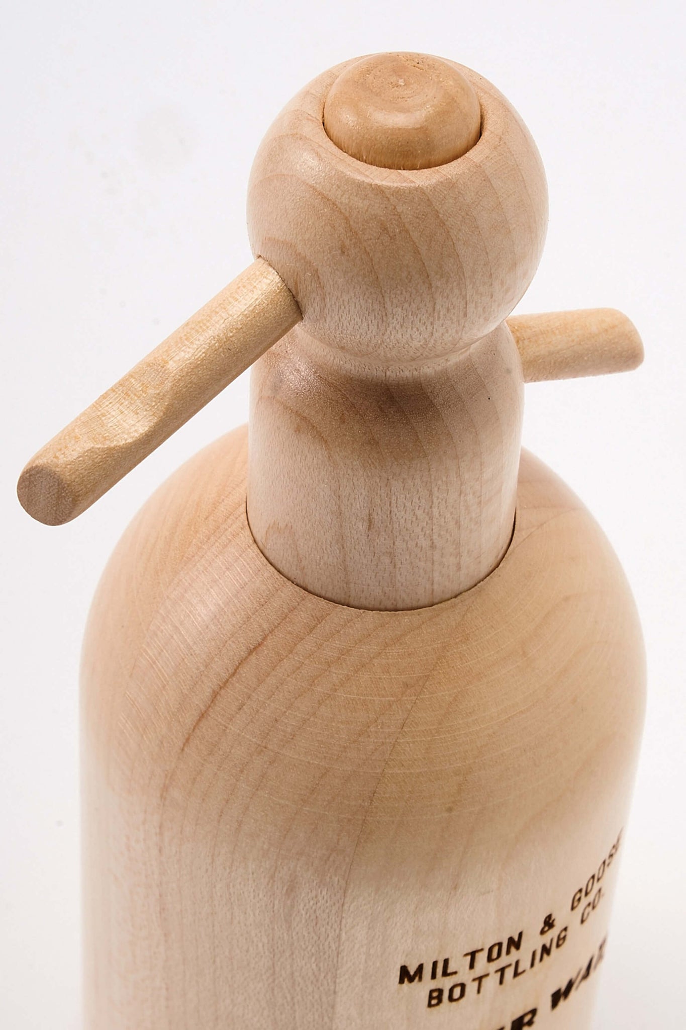 Close up of wooden seltzer bottle toy by Milton & Goose. Image is focused on the top push button and spout.