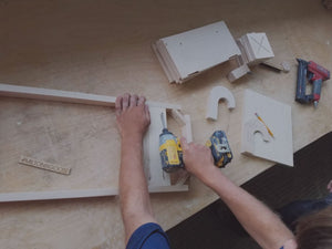 Milton and Goose Essential Play Kitchen in production. Person drilling base together with faucet template and wooden pieces sitting to the side.