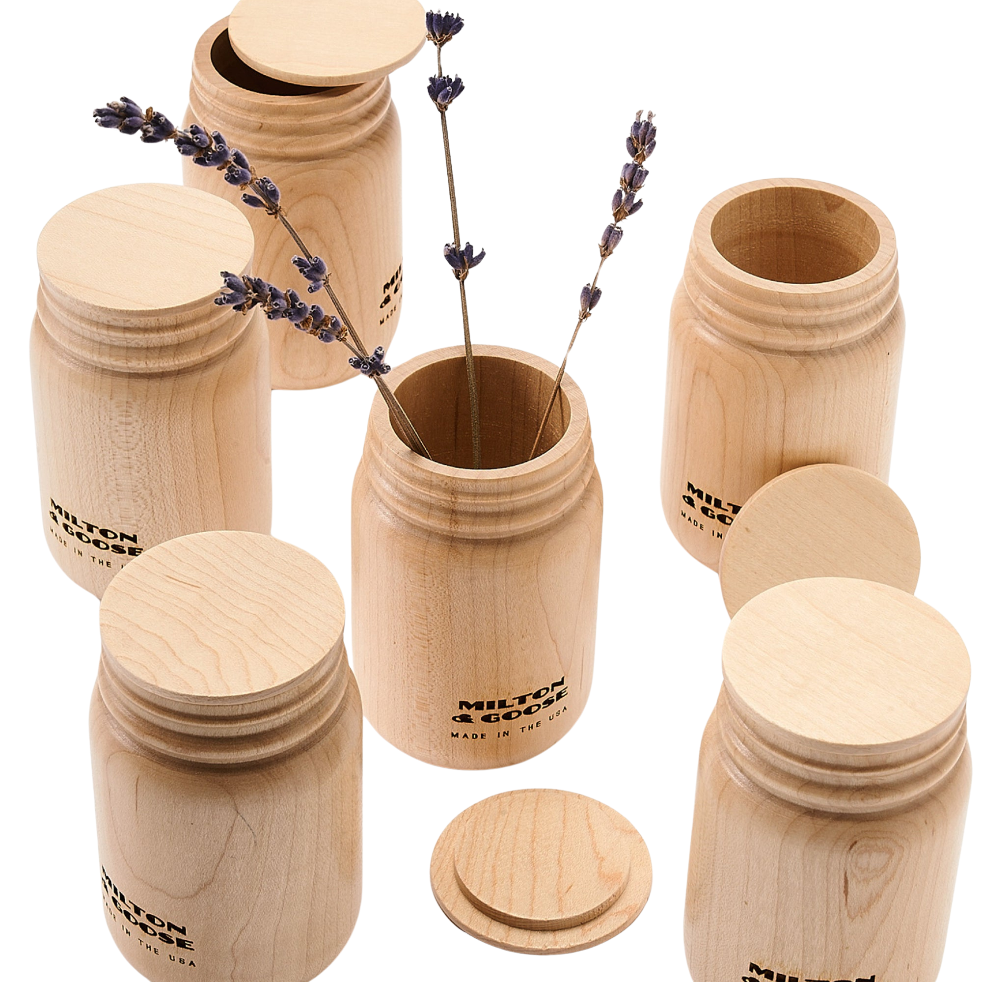 A group of wooden mason jars with flat lids. Jars are laser engraved and finished with a clear finish. One jar holds a sprig of lavendar.