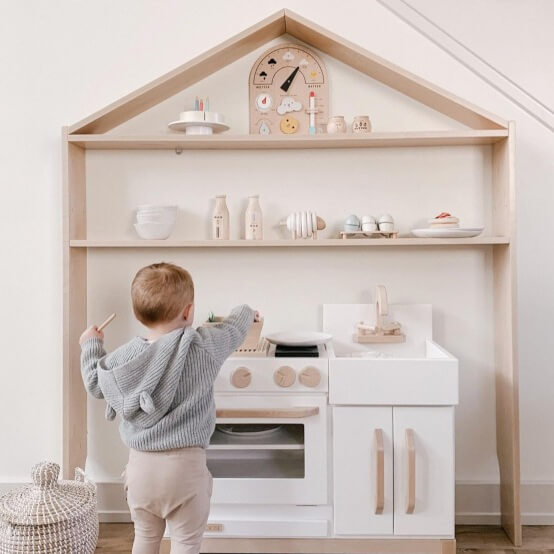 Milton and Goose wooden play kitchen with a house shelf sitting over it. Toddler plays at the kitchen.