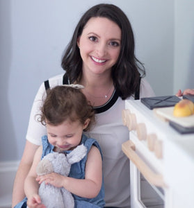 Milton & Goose's founder and CEO Shari Raymond sitting next to the Essential Play Kitchen in White with daughter on her lap.