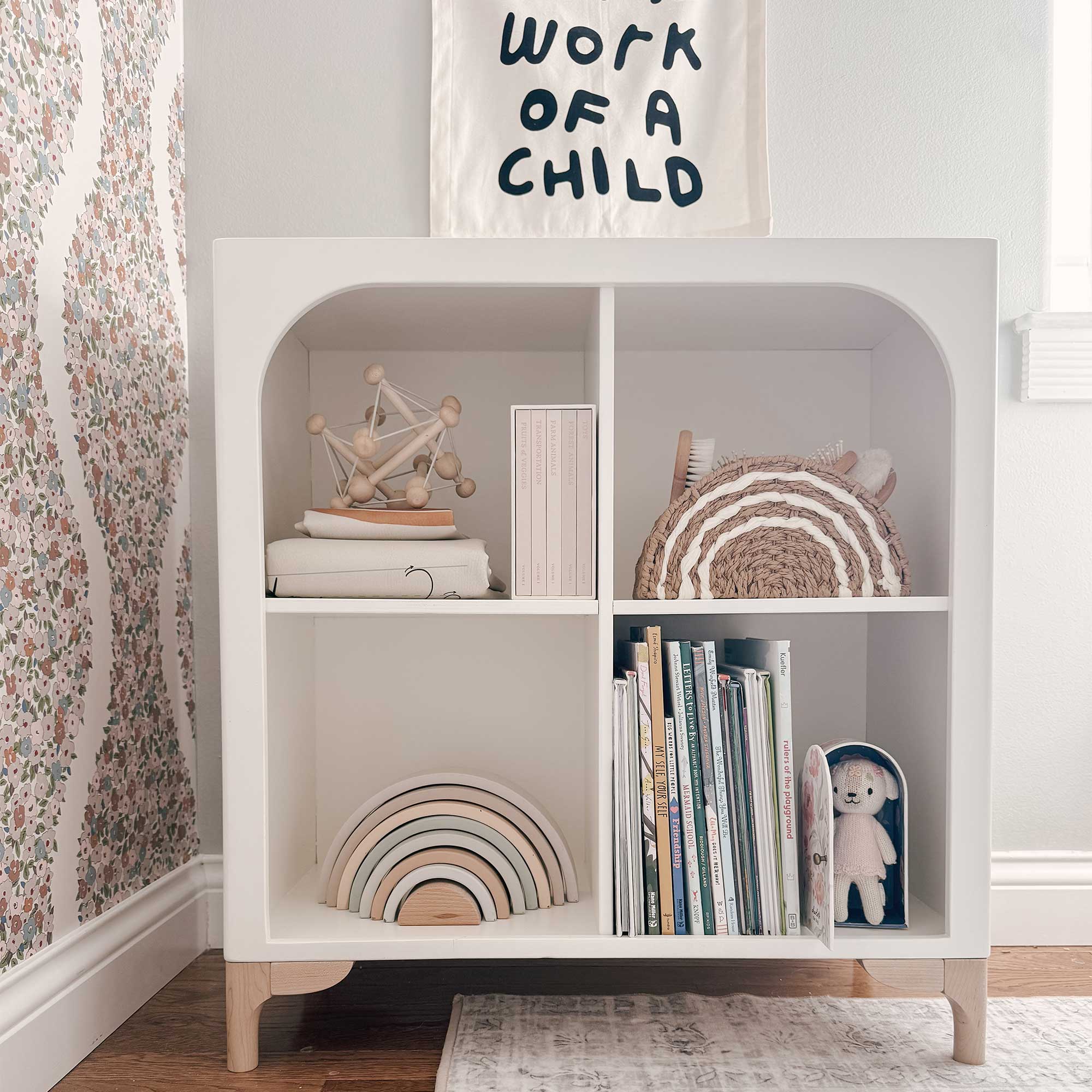 The wooden Archie Bookshelf by Milton & Goose is featured inside a nursery with baby toys and picture books stored inside. 