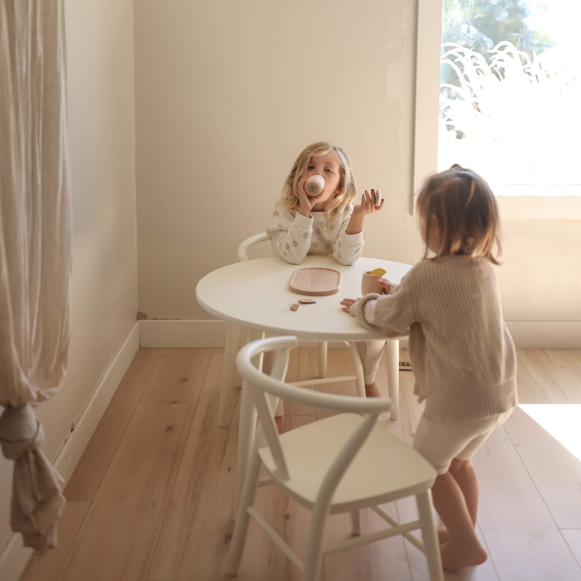 Two young children are seen having a tea party with the white round Crescent Table and white Crescent Chairs. 