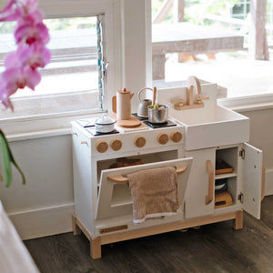 The wooden Essential Play Kitchen in White is shown with pretends pots and pans. 