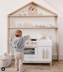 Child playing in front of Milton & Goose Essential Play kitchen in white. Kitchen set under the Milton & Goose House Shelf in Natural. Credit to IG profile @mandinelson_