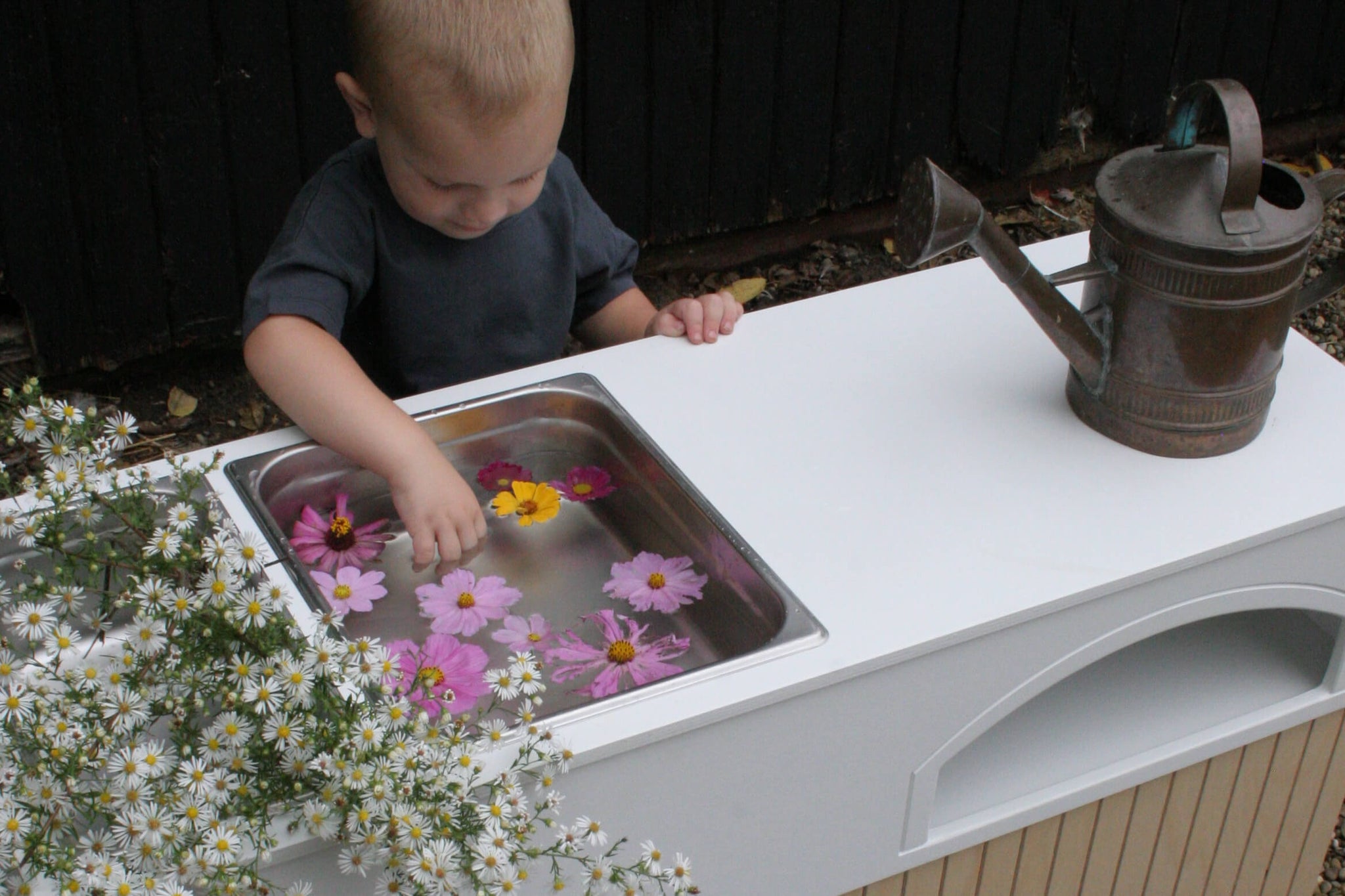 Toddler plays with flowers and water in the Milton & Goose Kai Mud Play Kitchen.