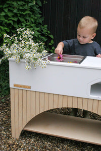 A toddler plays with flowers in the Milton & Goose Kai Mud Play Kitchen. 