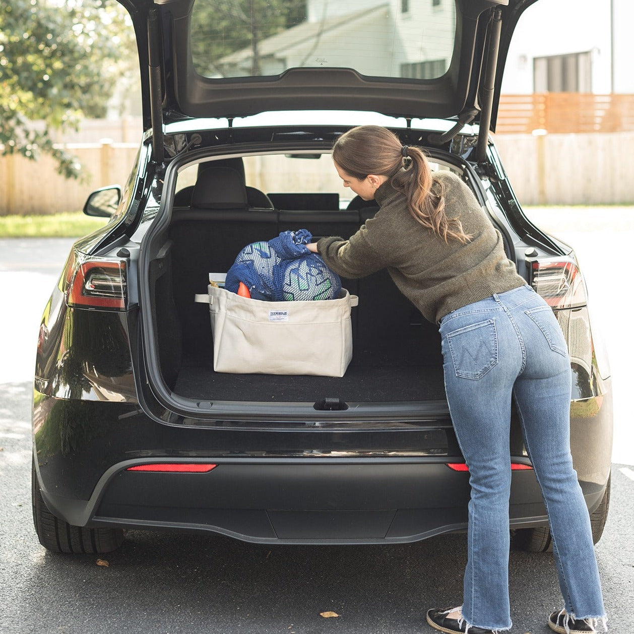 Person loading large canvas storage bins into the trunk of a car