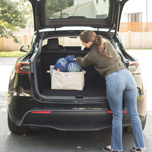 Person loading large canvas storage bins into the trunk of a car