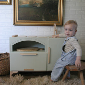 A child is shown playing with a green Luca Play Kitchen. 
