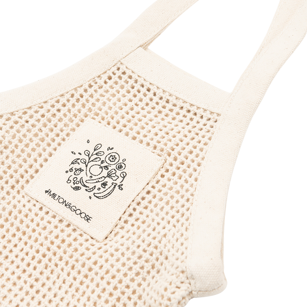 A child's mesh tote bag in a cream color with a picture of veggies and the Milton & Goose logo on the front.