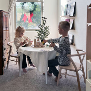 A boy and girl sit at their Milton & Goose round crescent table which is covered in the Milton & Goose tablecloth. 