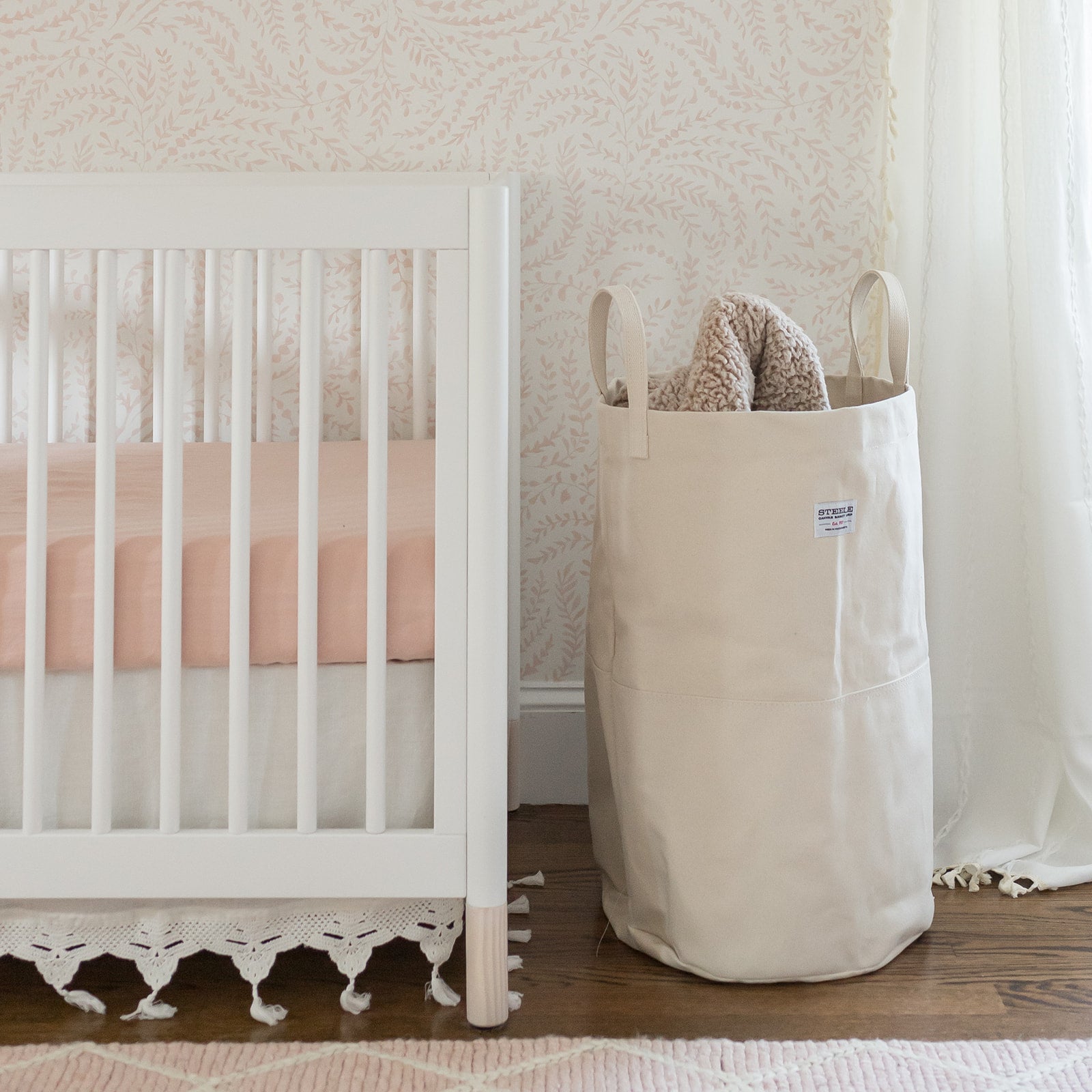 A tall canvas storage bin sits next to a white crib in a nursery.