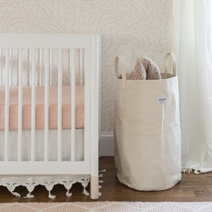 A tall canvas storage bin sits next to a white crib in a nursery.