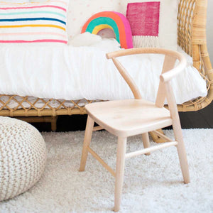 The Milton & Goose kid's Crescent wood Chair in natural is shown sitting in front of a child's bed.