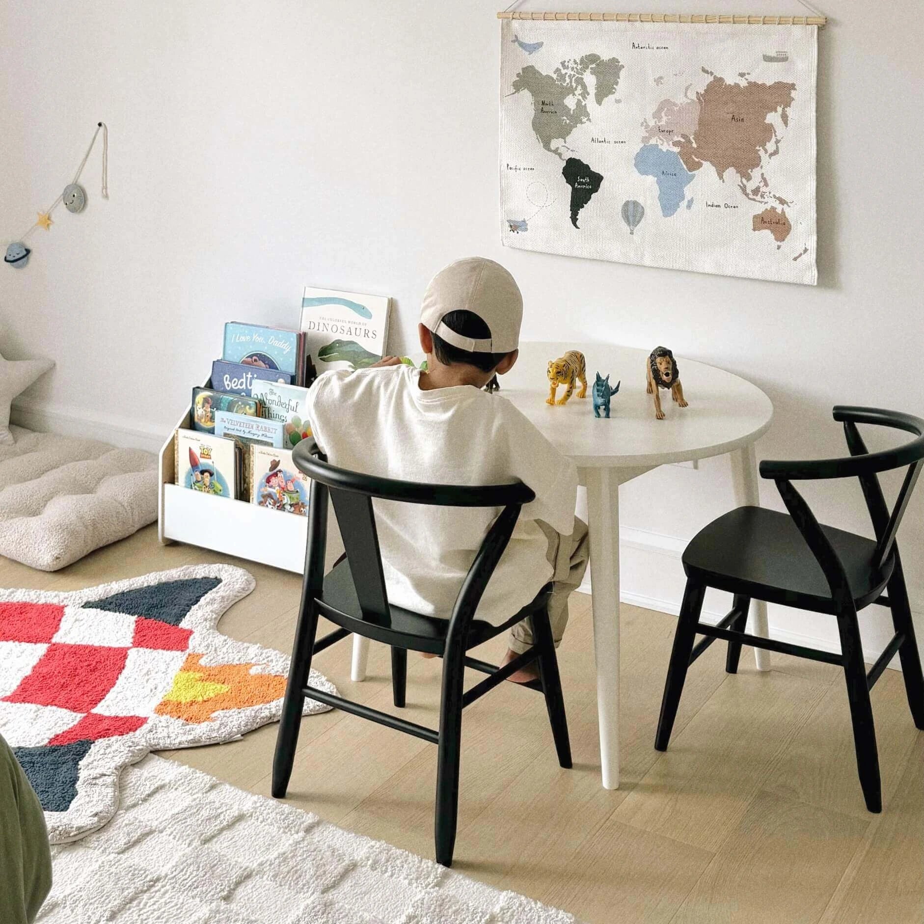 A young boy is shown playing while sitting on a black kid's wood Crescent Chair next to a white Crescent Round Table. 