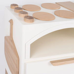 Milton & Goose Luca Wood Play Kitchen in white. Close up of pizza paddle on hanging on the left side, burners and oven knobs on the top of the stove.