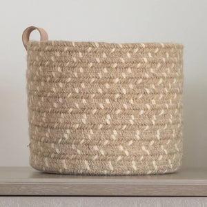 A closeup of the round braided basket with leather loop handle in beige.