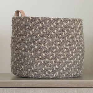 A closeup of the round braided basket with leather loop handle in dark gray.