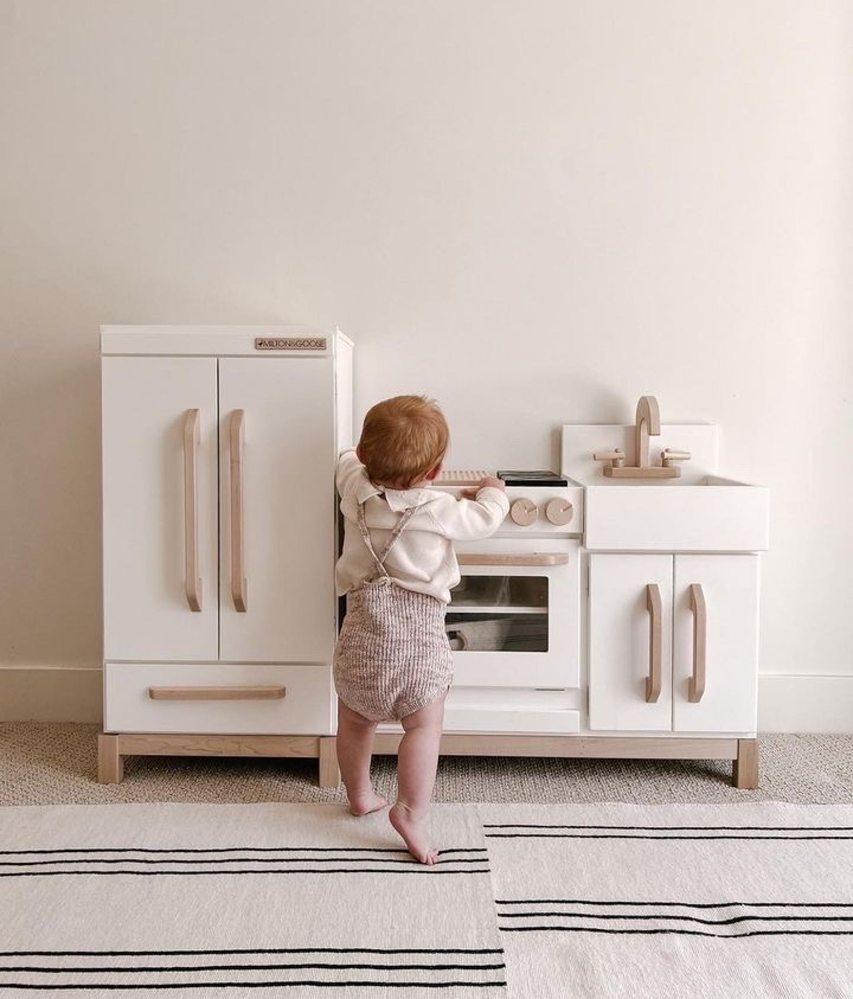 Baby plays with her wooden play kitchen and refrigerator from Milton & Goose.
