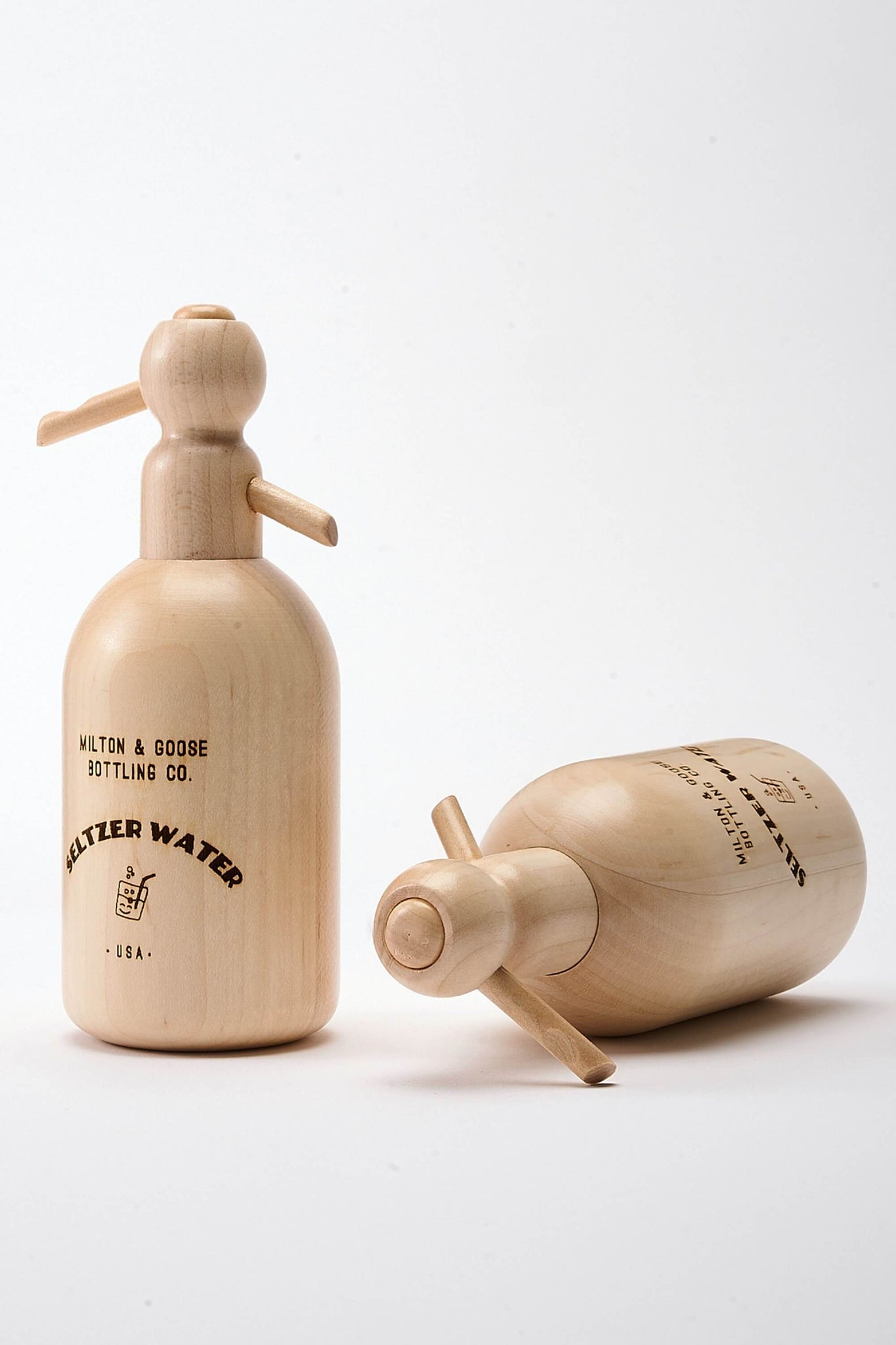 Two wooden Seltzer Bottle Toys. One is standing and one is laying on its side.