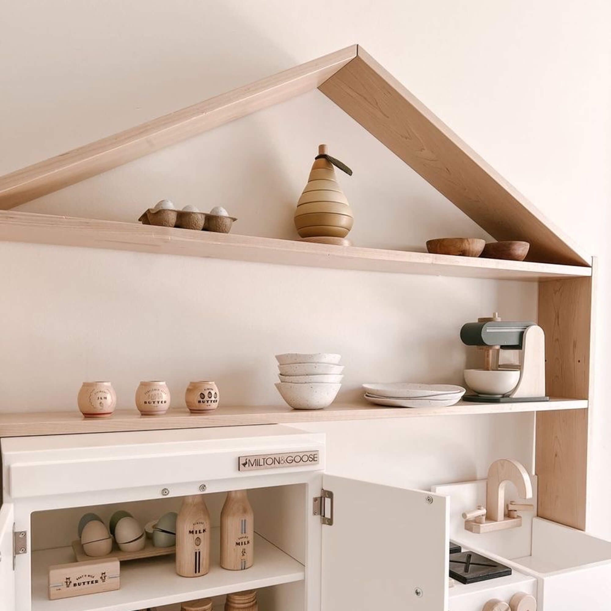 A close up view of the wooden house shaped shelf over the essential play kitchen and refrigerator.